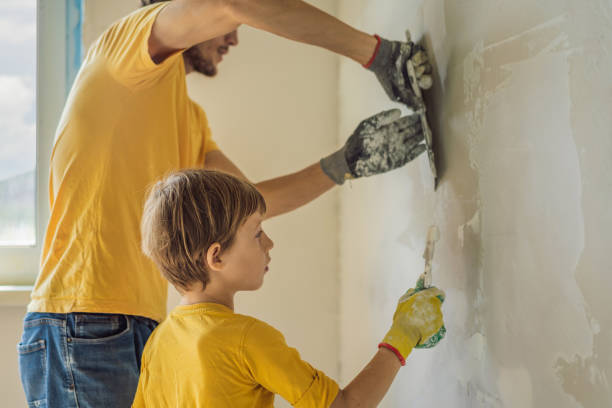 man with his son makes repairs at home, he teaches children to plaster the walls with a spatula in his hands - plaster plasterer work tool child foto e immagini stock