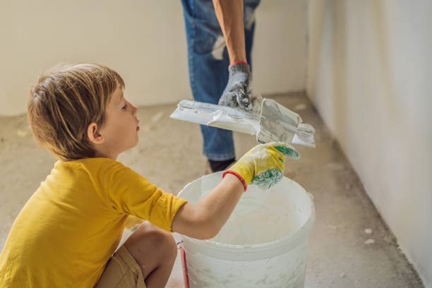 man with his son makes repairs at home, he teaches children to plaster the walls with a spatula in his hands - plaster plasterer work tool child foto e immagini stock