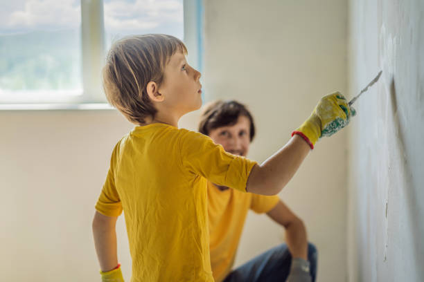man with his son makes repairs at home, he teaches children to plaster the walls with a spatula in his hands - plaster plasterer work tool child foto e immagini stock