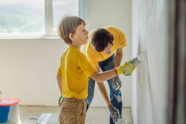 man with his son makes repairs at home, he teaches children to plaster the walls with a spatula in his hands - plaster plasterer work tool child foto e immagini stock