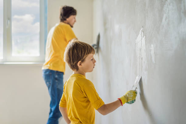 man with his son makes repairs at home, he teaches children to plaster the walls with a spatula in his hands - plaster plasterer work tool child foto e immagini stock