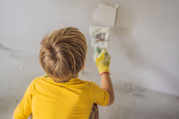 boy makes repairs at home, he teaches children to plaster the walls with a spatula in his hands - plaster plasterer work tool child imagens e fotografias de stock