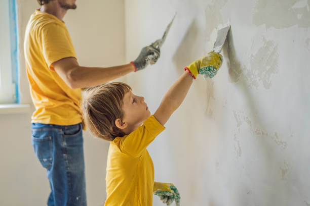 man with his son makes repairs at home, he teaches children to plaster the walls with a spatula in his hands - plaster plasterer work tool child foto e immagini stock