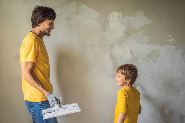 man with his son makes repairs at home, he teaches children to plaster the walls with a spatula in his hands - plaster plasterer work tool child foto e immagini stock