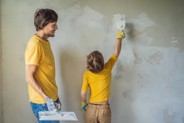 man with his son makes repairs at home, he teaches children to plaster the walls with a spatula in his hands - plaster plasterer work tool child foto e immagini stock