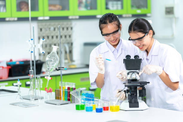 due scienziate asiatiche sono dottoresse nella facoltà di medicina. fai ricerche e tieni una provetta attraverso un microscopio. produrre vaccini e medicinali per curare i virus. bicchiere nel laboratorio di biologia - test tube biologist laboratory beaker foto e immagini stock