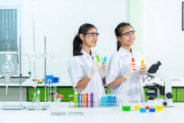 laboratorio di biologia di un ospedale in un'organizzazione aziendale c'è una presentatrice femminile che è un medico in piedi e tiene in mano una provetta, ricerca farmaci e ha un microscopio e un becher. - test tube biologist laboratory beaker foto e immagini stock