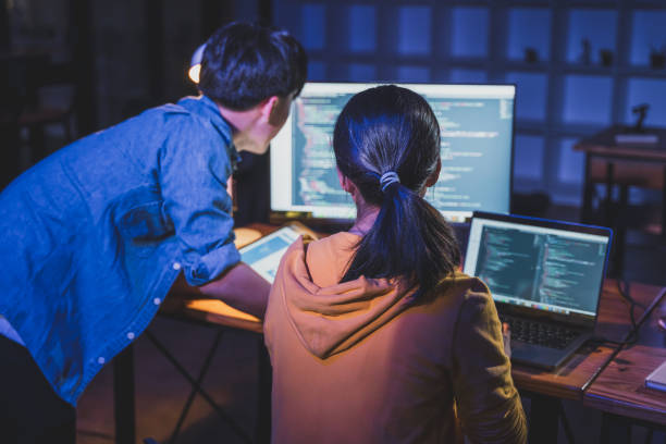 istock Two young male and female  programmers working on their coding together late at night in their office with dramatic warm and cool lighting 2042222715