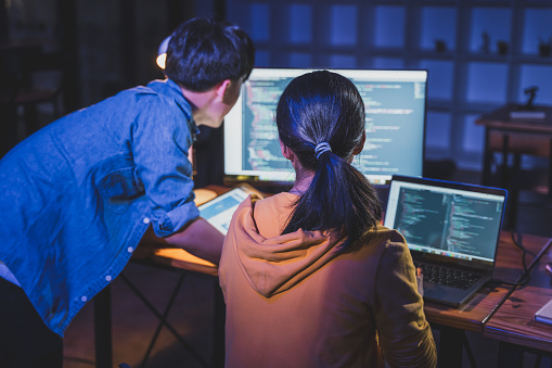 Two young male and female  programmers working on their coding together late at night in their office with dramatic warm and cool lighting