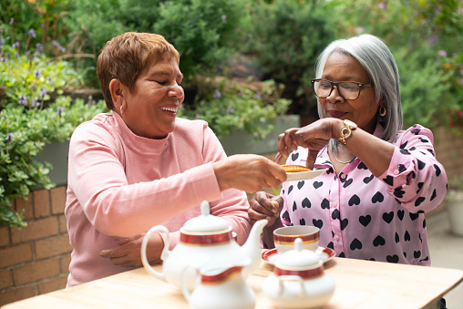 Senior, women and friends with tea outdoor in garden of home for retirement, relax and biscuit in backyard. Elderly, people and hot beverage in nature for bonding, happiness and conversation by table