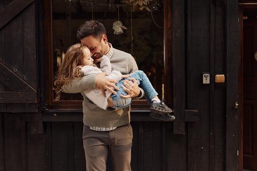 Happy single father having fun with his small daughter in front of the house.