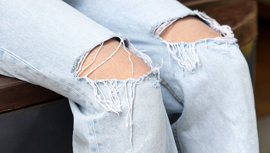 Close up of jeans with torn edges. Woman's legs in jeans.