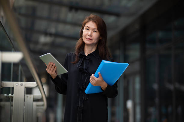 istock Asian business woman holding document folder and using digital tablet at financial district 2042264197