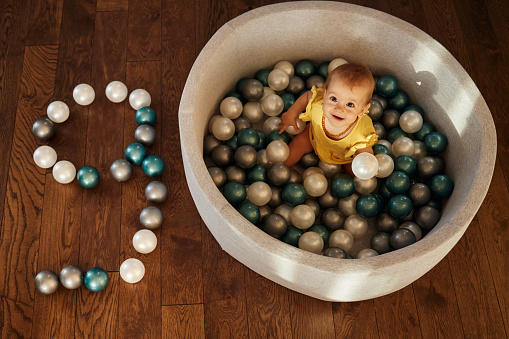 High angle view of happy baby girl sitting inside of pool ball by the number 9 made of balls.