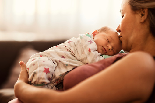 Cute newborn baby sleeping in her mother's arms while she is kissing her. Copy space.