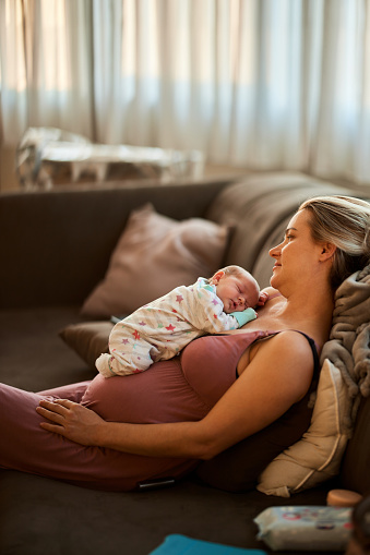 Cute newborn baby sleeping on her single mother in the living room. Copy space.