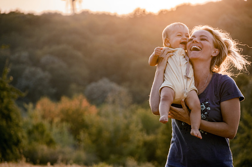 Cheerful single mother and her baby girl having fun in the park at sunset. Copy space.