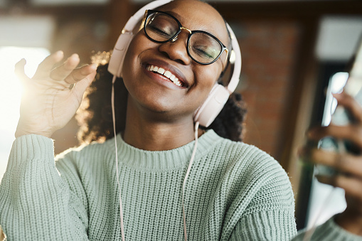 Happy African American woman having fun while listening music over headphones at home.