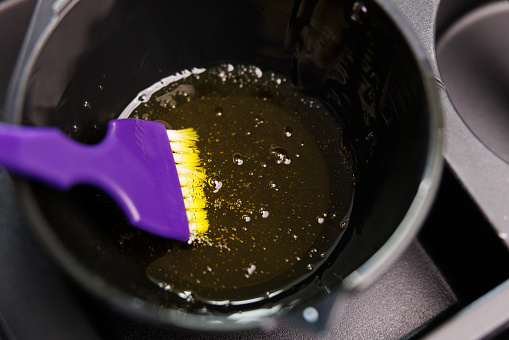 A purple brush is immersed in a pot of liquid, possibly an ingredient for a recipe or drink. The fluid could be part of a cooking dish or mixture in a circle cuisine