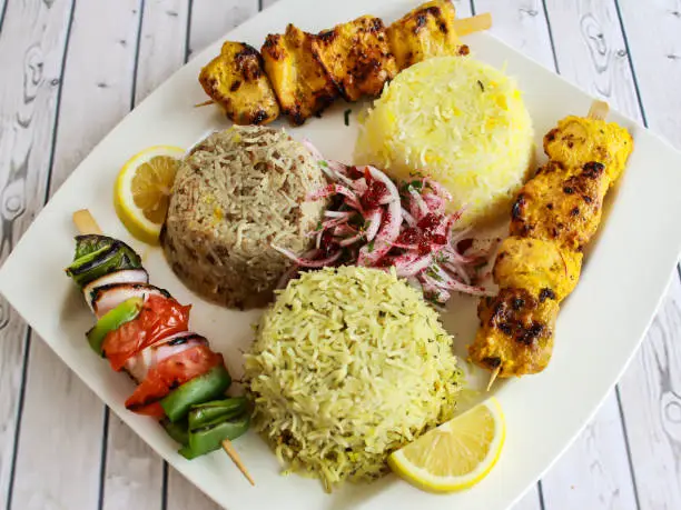 Photo of Chicken Joojeh Kebab Rice with onion, lemon served in dish isolated on table closeup top vie of arabic spicy food