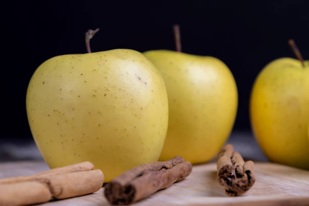 Ripe organic red apple, leaves, cinnamon stick on wooden table background. Autumn composition.