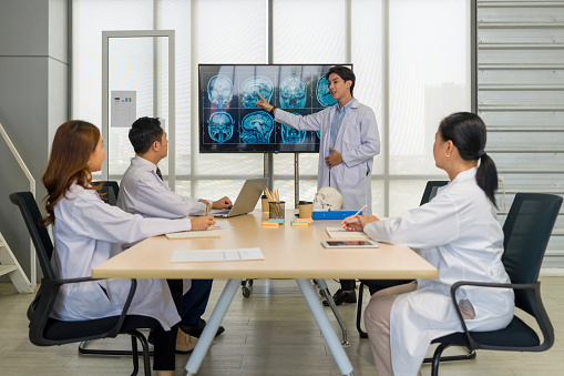 Group of doctor in white gown, discussing brain scans on large monitor in a meeting room.