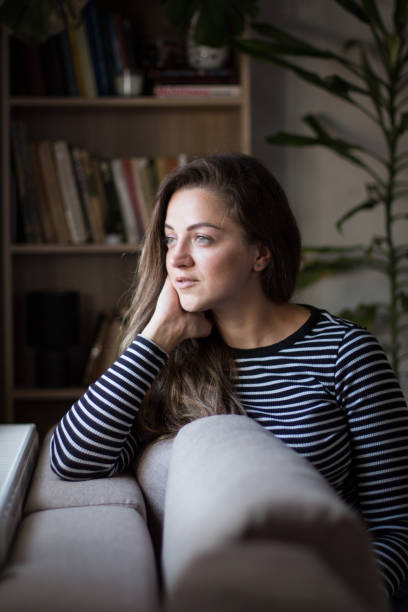istock Young woman sitting by the window, relaxing on her couch. 2042428185