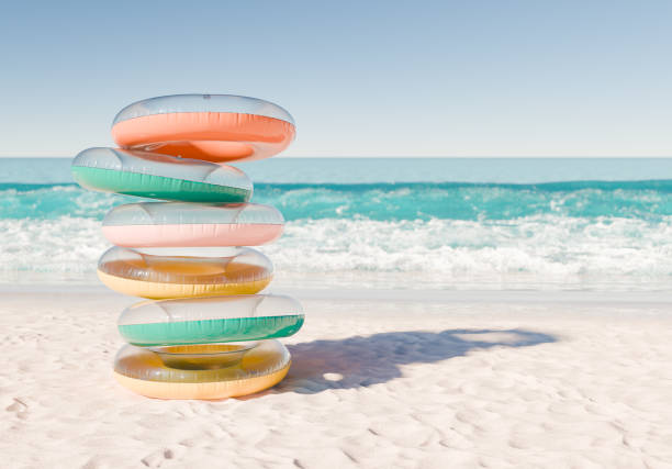 3D rendering of a stack of multicolored swim rings on a white sandy beach with ocean waves in the background. Fun and leisurely summer day.