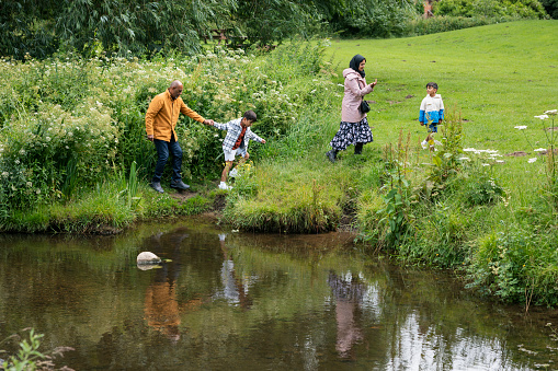A mature couple enjoying a day outdoors in a public park in Ponteland, North East England with their grandchildren. They are walking away from a river's edge after looking at the wildlife in the water.