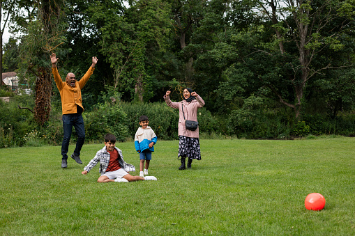 A mature couple enjoying a day outdoors in a public park in Ponteland, North East England with their grandchildren. They are playing football on a grass area and cheering together after having a great game.