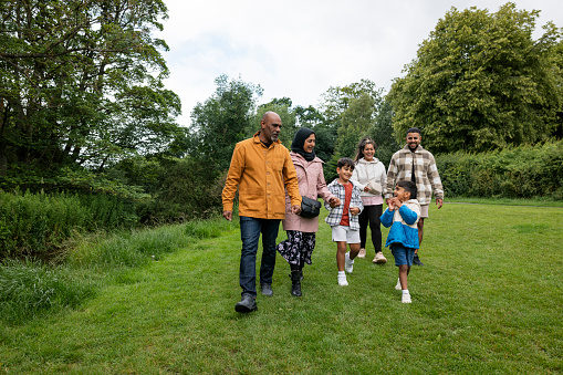 A multi-generation family enjoying a day outdoors in a public park in Ponteland, North East England. They are walking on a grass area while they bond with each other.