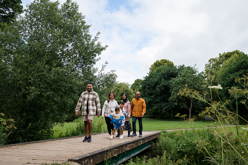 A multi-generation family enjoying a day outdoors in a public park in Ponteland, North East England. They are walking over a bridge across a river while bonding and smiling.