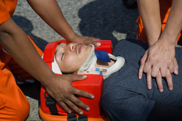 istock A man in head immobilizer tool lying on stretcher long spinal board with safety belt get CPR from rescue team. Urgent assistance during road accident. 2042493838