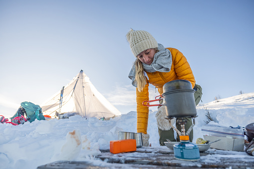 Female on a snowshoeing cross country adventure prepares food at her camp in the snow. Camping in extreme conditions