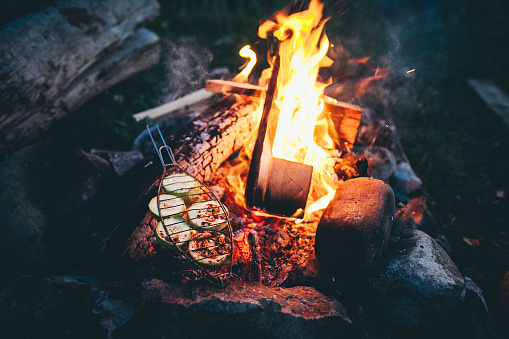 A campfire crackling in the darkness, flames dancing and heat glowing, with a shovel sticking out of the bonfire, adding to the cozy atmosphere