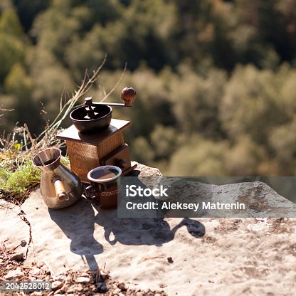 Toy coffee grinder rests on bedrock next to two cups in the landscape