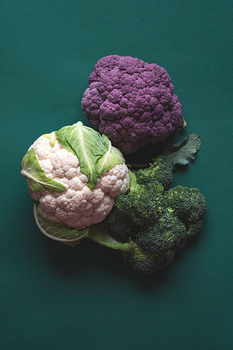 Cruciferous cabbages: broccoli, cauliflower and purple cabbage on a green emerald background. Vegetables full of vitamins and minerals, healthy food, farm products, top view