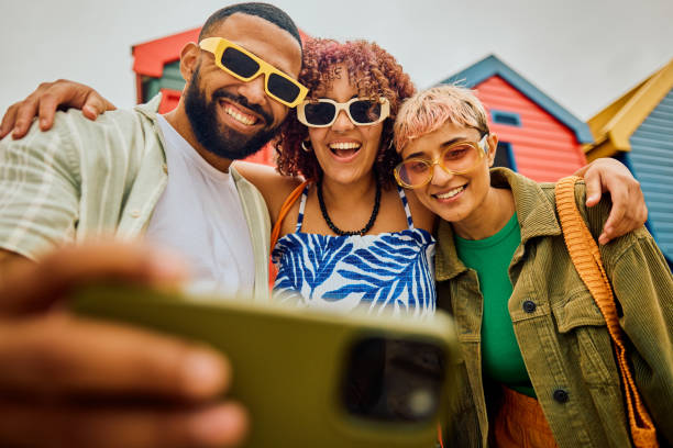 Happy group of friends using their smartphone while travelling. Taking photos, looking for directions and checking their hotel bookings together on a phone. stylish selfie stock pictures, royalty-free photos & images