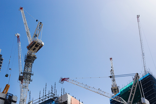 Several cranes over an active construction site, building skyscrapers, clear blue sky.