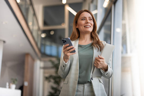 smiling businesswoman using phone in office - affärsmänniska bildbanksfoton och bilder