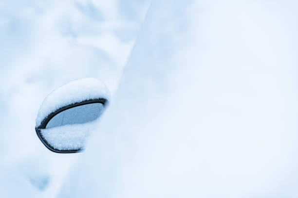 A cars side mirror is enveloped by a blanket of fresh snow, reflecting the chilly winter atmosphere in Sweden. The vehicle appears stationary, coated with snowflakes, emphasizing the cold, serene, and snowy conditions of the day.