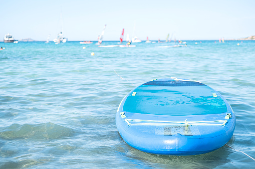 Lonely blue sup board on the sea on floating sailboats background on sunny day.