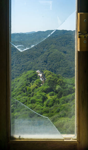 istock View through a broken glass window of a monastery surrounded by trees and mountains. The bell tower, defensive tower and church are visible. 2042590489