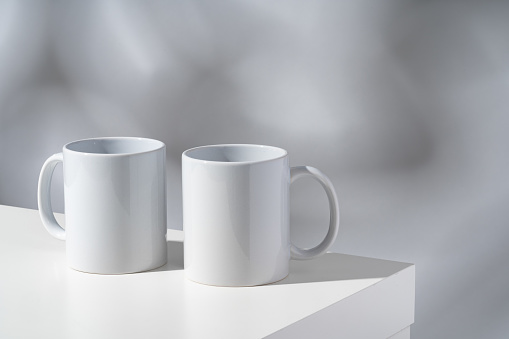 White ceramic mugs on gray background with shadows mock up