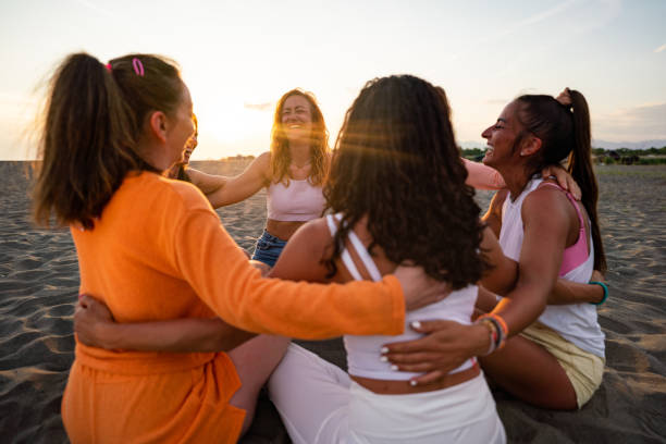 A group of happy women support each other while sitting on the beach during a summer day