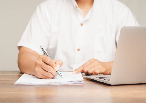 istock A businessman is holding a pen and writing in a document while sitting at a desk. 2042613947