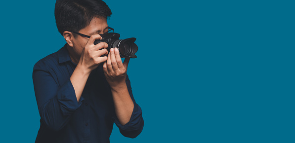 Photographer with a camera. Tomboy's holding the digital camera while standing on a blue background. Tomboy is a girl who loves to be a man. LGBT. Gender diversity and the photography concept