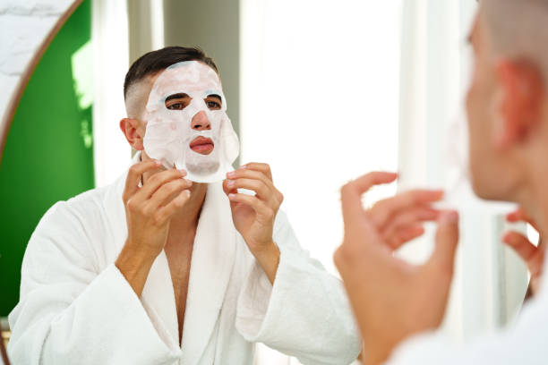 istock Handsome young man applying sheet mask near mirror in bathroom 2042635860