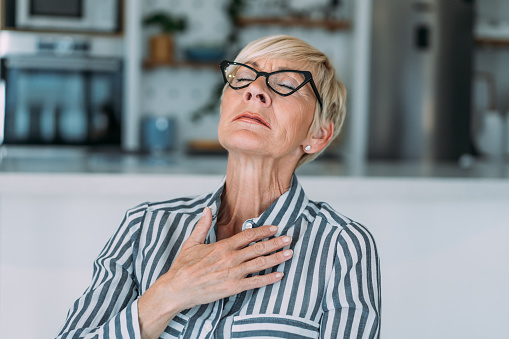 Shot of worried mature woman feeling unwell and having chest pain in the living room.