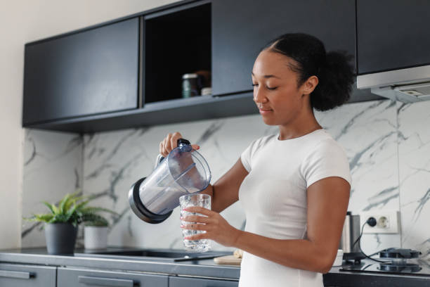 istock Young Woman Pouring Water into Glass in Kitchen 2042654578